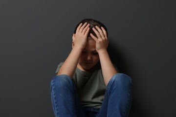 Child abuse. Upset girl sitting on floor near grey wall