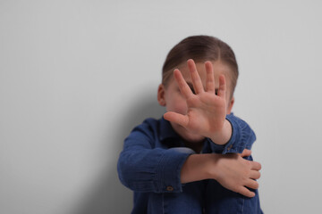 Child abuse. Girl making stop gesture near grey wall, selective focus. Space for text