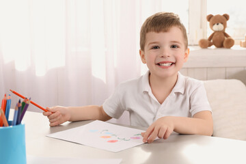 Cute little boy drawing with pencil at light table in room. Child`s art