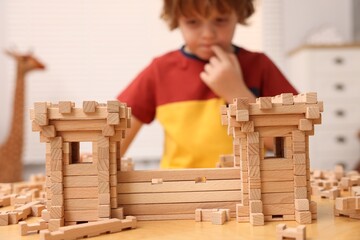 Little boy playing with wooden construction set at table in room, selective focus. Child's toy