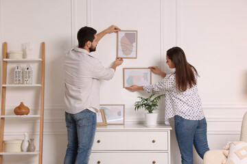 Man and woman hanging picture frames on white wall at home