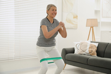 Senior woman doing squats with fitness elastic band at home