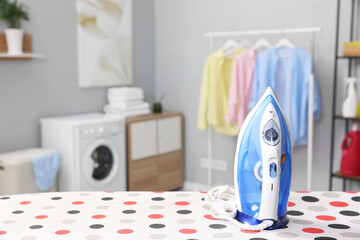 Clothes iron on ironing board in laundry room, space for text