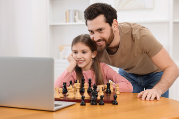 Father teaching his daughter to play chess following online lesson at home