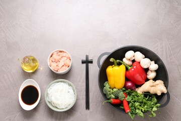 Wok, chopsticks and different products on grey textured table, flat lay. Space for text