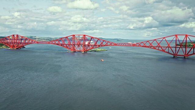 Aerial view of Forth Bridge, a long red railway bridge crossing the Forth estuary. Cantilever railway bridge carrying passengers and freight, cruise ship transporting tourists in Scotland.