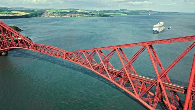 Aerial view of Forth Bridge, a long red railway bridge crossing the Forth estuary. Cantilever railway bridge carrying passengers and freight, cruise ship transporting tourists in Scotland.