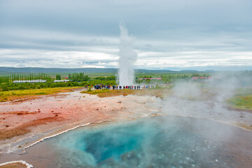 Geyser, Iceland - August 18, 2015: Geysir in South Iceland, at Strokkur, Golden Circle, at summer with dramatic sky and tourists watching the geyser, red volcanic soil. © neurobite