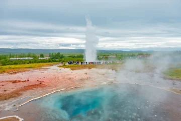 Dekokissen Geyser, Iceland - August 18, 2015: Geysir in South Iceland, at Strokkur, Golden Circle, at summer with dramatic sky and tourists watching the geyser, red volcanic soil. © neurobite