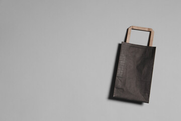 One black paper shopping bag on grey background, top view. Space for text