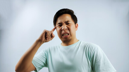 Portrait of Asian Man in blue T- shirt, index finger towards head making thinking gesture isolated...