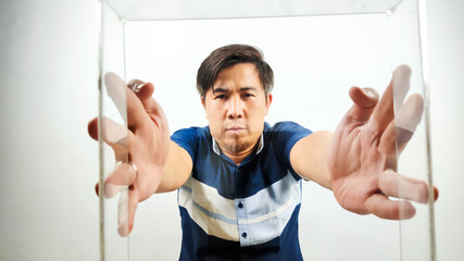 Portrait of Asian Man in blue and white shirt holding transparent box and trying to see the other...