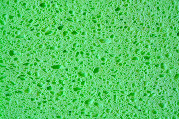 Green sponge with pores texture background for graphics. Close-up macro photo of household sponge tissue.