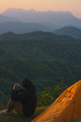 nature traveling with orange camping tent and layer of mountain with solo man drink coffee and see sunrise