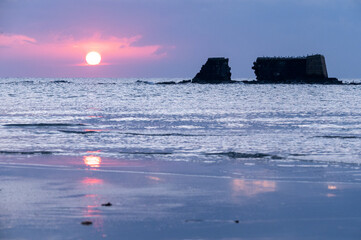 Alba sul mare con riflesso del sole sulla sull'acqua e sulla sabbia.