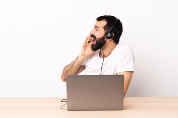 Telemarketer caucasian man working with a headset and with laptop shouting with mouth wide open to the side.