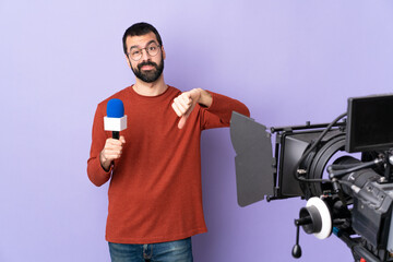 Reporter man holding a microphone and reporting news over isolated purple background showing thumb down with negative expression