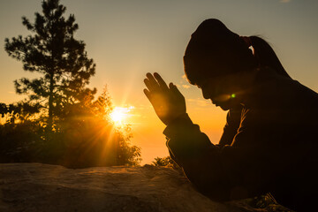 Woman kneeling to pray on Easter Day. Silhouette of prayer woman kneeling and praying over autumn...