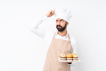 Young man holding muffin cake over isolated white background having doubts while scratching head