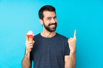 Young man with a cornet ice cream over isolated blue background pointing up a great idea