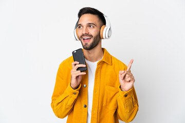 Young caucasian man isolated on white background listening music with a mobile and singing