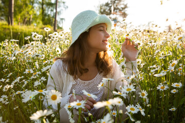 Girl sitting on a meadow covered with wild flowers. Background of field of daisy flowers in bloom....