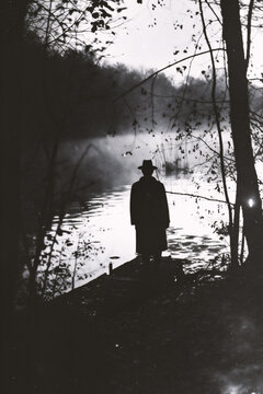 A silhouette of a man standing by the river. Black and white photo