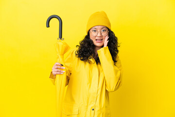 Asian woman with rainproof coat and umbrella isolated on yellow background with surprise and...