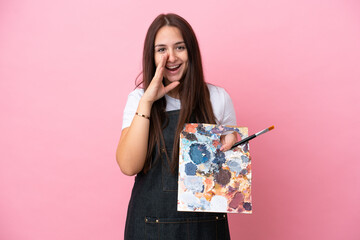Young artist Ukrainian woman holding a palette isolated on oink background shouting with mouth wide...