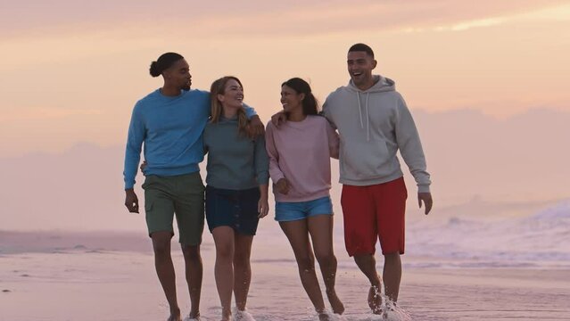 Young couple with friends wearing casual clothing hugging as they walk towards camera along beach at dawn - shot in slow motion