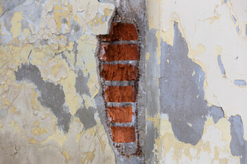 Collapsed red bricks and peeling plaster on the wall of a house with yellow walls close up