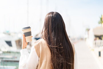 Young Chinese woman holding a take away coffee at outdoors in back position
