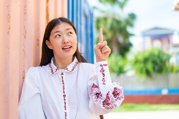 Young Chinese woman at outdoors intending to realizes the solution while lifting a finger up