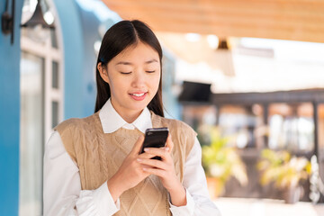 Young Chinese woman at outdoors sending a message or email with the mobile