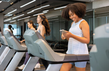 Young African American woman exercising on  treadmill at a gym.Woman Chat and texting mobile on...