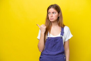 Young caucasian woman isolated on yellow background unhappy and pointing to the side