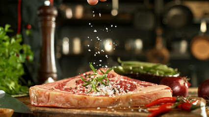 Close-up of falling salt on tasty beef steak in kitchen. Chef in background.