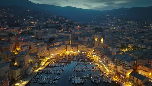 Flying over evening Bastia with city lights, Corsica island. Aerial view of Bastia harbor with yacht and old town, mediterranean sea, Corsica, France