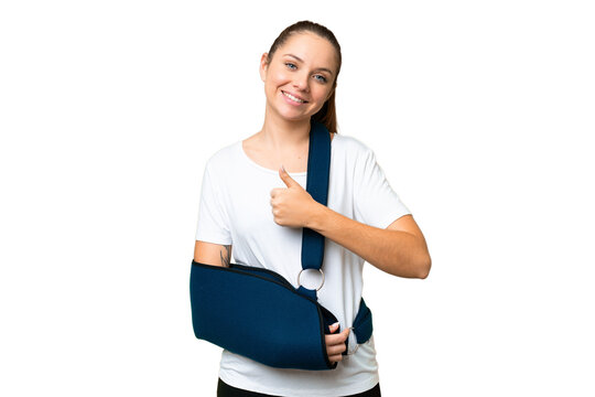Young blonde woman with broken arm and wearing a sling over isolated chroma key background giving a thumbs up gesture