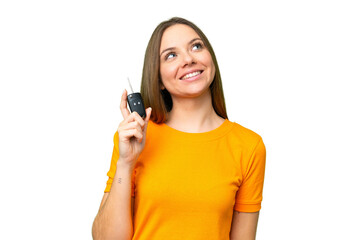 Young woman holding car keys over isolated chroma key background looking up while smiling