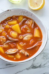 Bowl of manhattan chowder with littleneck clams, vertical shot on a white marble background, middle close-up, selective focus