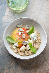 Grey bowl with pear and blue cheese risotto, vertical shot on a beige and grey granite background, high angle view