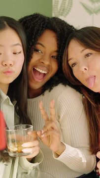 Multiracial women pulling funny faces while taking a selfie indoors