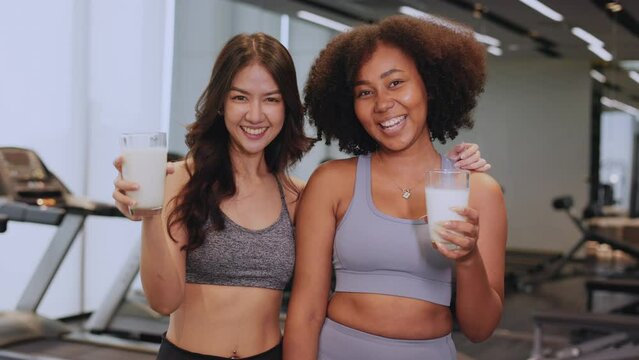Asian and African American woman finishing workout and drinking protein milk shake vitamins after training. Bodybuilding. Healthy Friend lifestyle.