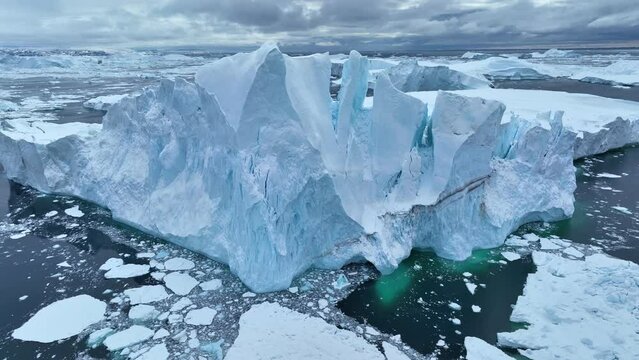 Flying over giant iceberg near Ilulissat, Greenland. Iceberg pieces break off and fall into the water. Aerial arctic nature landscape, global warming and climate change concept