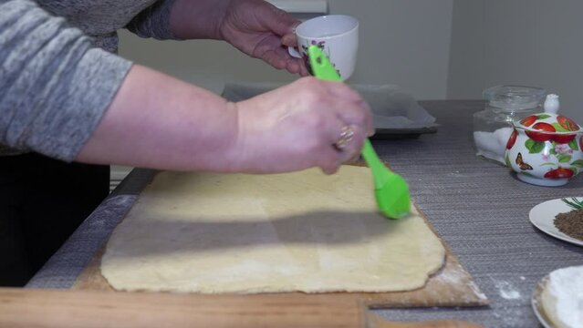 a woman smears the dough with eggs, a woman in the kitchen brushes cookie dough