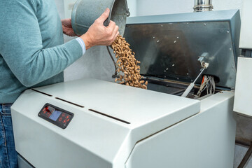 Man filling a biomass boiler or stove with wood pellets. Biofuel heating system at home.
