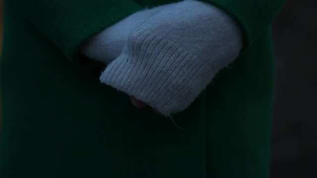 Close-up view of frozen woman hands. Female covers cold hands with sweater and tries to warm them. Hands turning red and blue from the freezing weather. Late evening light.