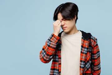 Young sad sick ill tired upset man of Asian ethnicity he wearing red hoody casual clothes keep eyes closed rub put hand on nose isolated on plain pastel light blue cyan background. Lifestyle concept.