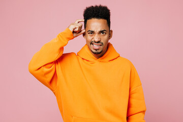 Young sad mistaken puzzled man of African American ethnicity he wears yellow hoody casual clothes look camera scratch hold head isolated on plain pastel light pink background studio Lifestyle concept